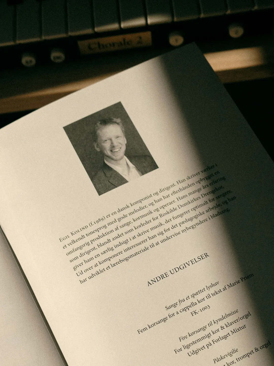 Black-and-white portrait of a smiling man above a Danish biography paragraph, resting near organ manuals.